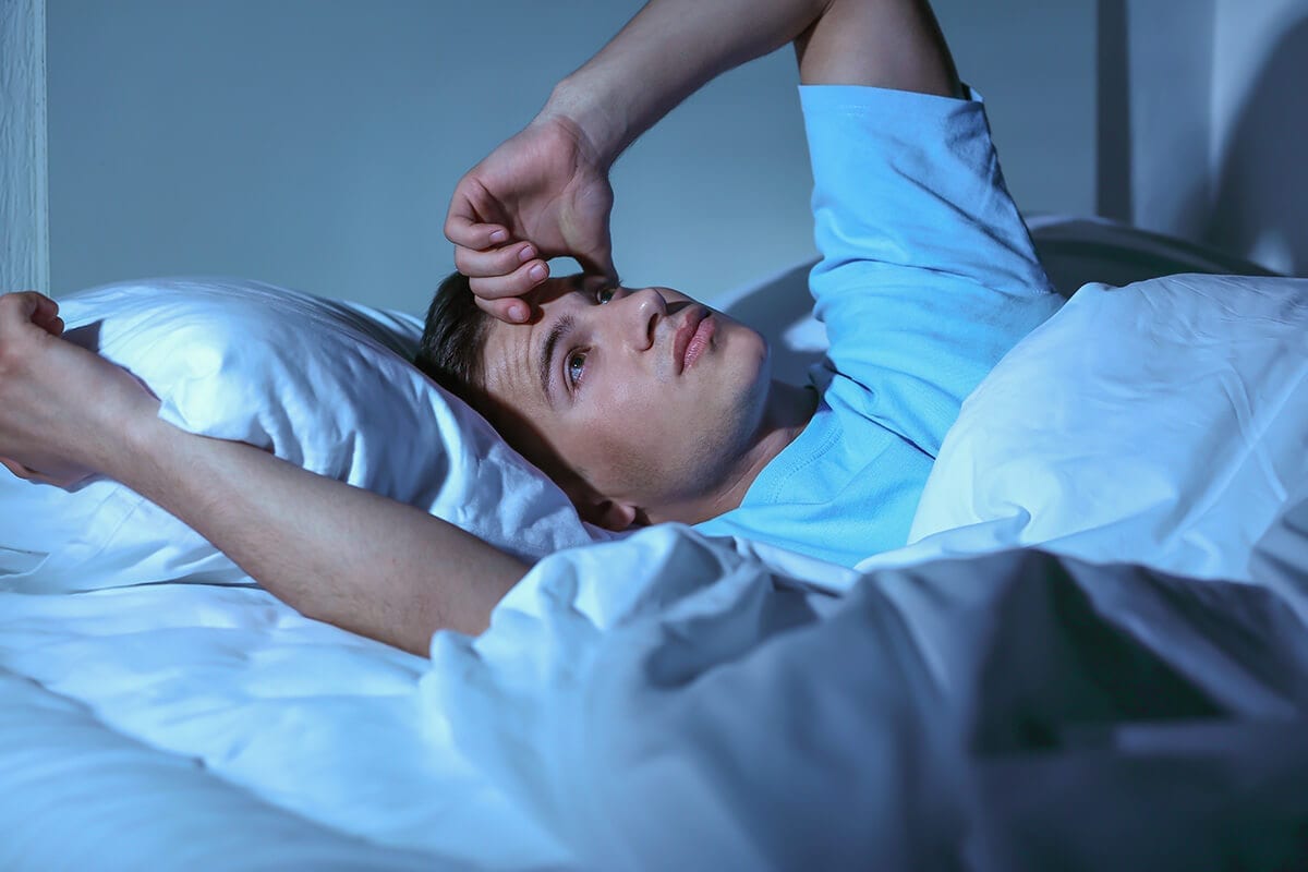 man laying awake blue bed